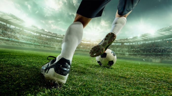 Faceless soccer player in white socks striking ball with power on green 3D stadium field